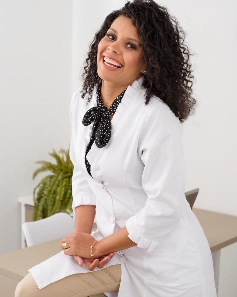 Odete Silva sorrindo, de jaleco branco, em ambiente de clínica de estética